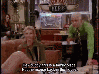 a man in a green shirt is standing next to a woman sitting on a couch in a restaurant .