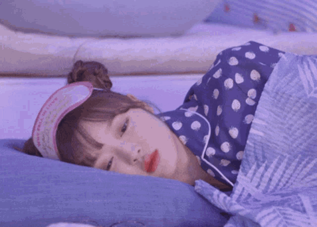 a girl wearing a sleep mask is sleeping on a purple blanket