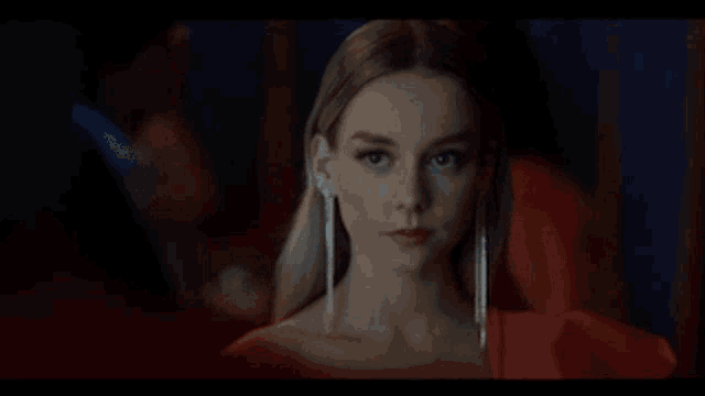 a woman in a red dress is looking at the camera in a dark room .