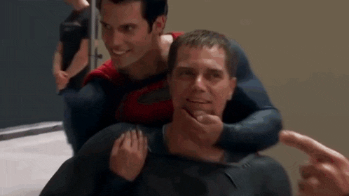 a man in a superman costume is holding another man 's neck and smiling .