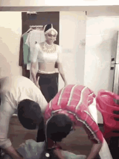 a woman in a white top and black pants is standing in a room surrounded by people