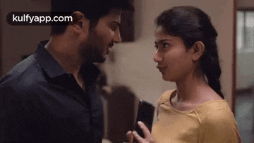a man and a woman are looking into each other 's eyes while a man holds a cell phone .