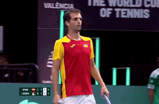 a man in a red and yellow shirt is holding a tennis racket in front of a sign that says the world cup of tennis