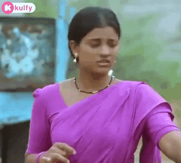 a woman in a purple saree is standing in front of a television screen .