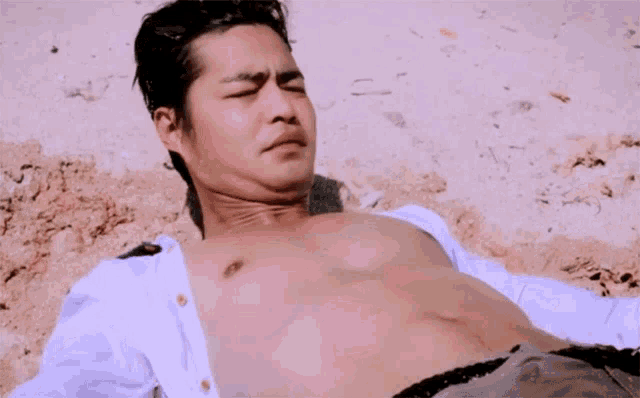 a shirtless man laying on a beach with his shirt off