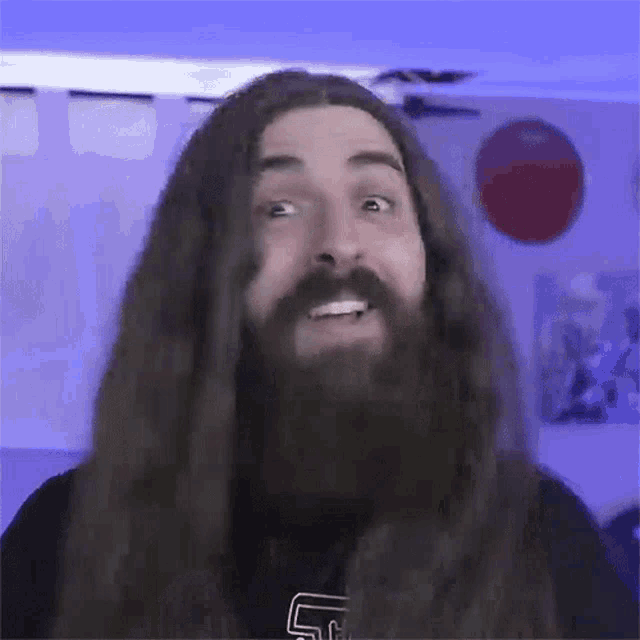 a man with long hair and a beard is wearing a shirt with the letter s on it .