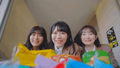 three girls are smiling and holding bags of snacks including one that says ' potato chips ' on it