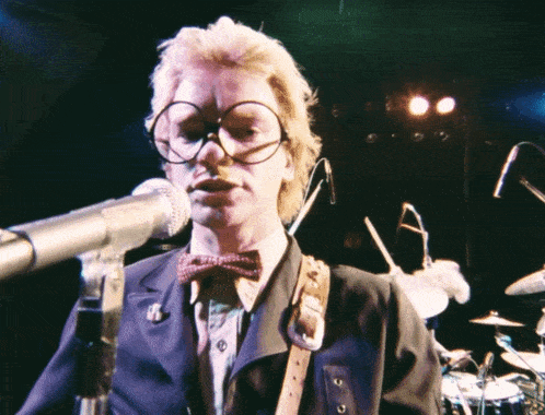 a man wearing glasses and a bow tie stands in front of a microphone