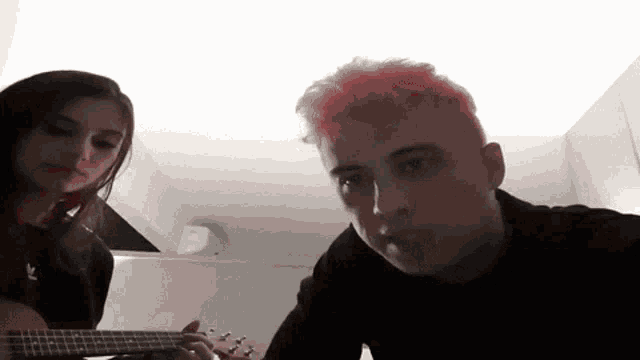 a man with pink hair playing a guitar next to a girl