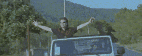 a man wearing sunglasses is standing in a field looking up at the sky .