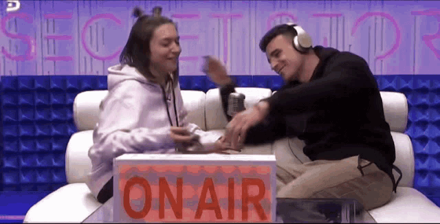 a man and a woman are sitting on a couch in front of an on air sign