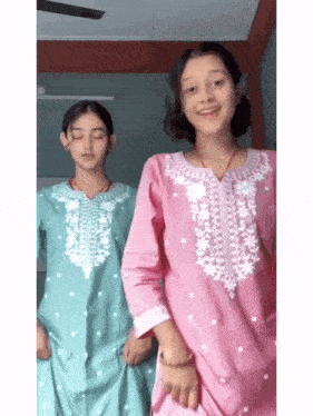 two young girls are standing next to each other in a room and dancing .