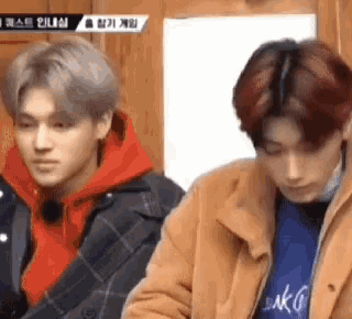 two young men are standing next to each other in a room . one of the men is wearing a red hoodie .