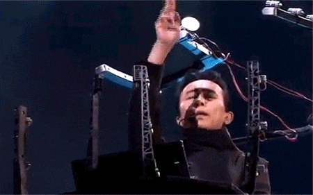 a man is playing a keyboard and singing into a microphone while standing on a stage .