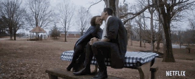 a man and a woman kissing on a picnic table with netflix written on the bottom