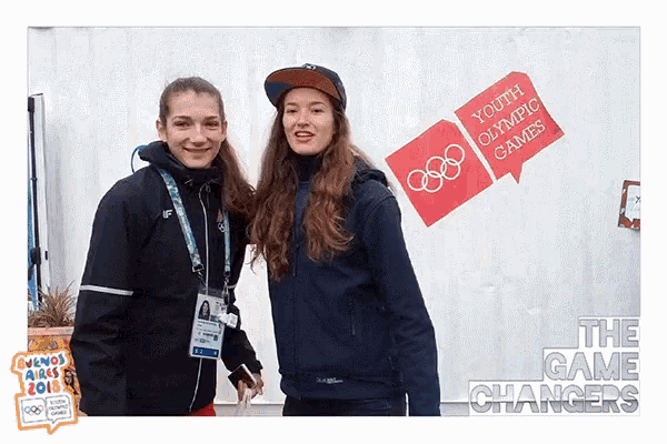 two young women pose for a photo in front of a sign that says youth olympic games
