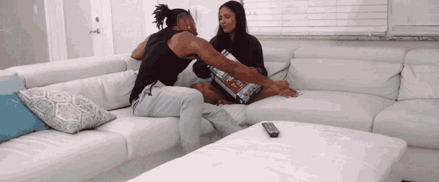 a man and a woman sit on a couch with a bag of chips