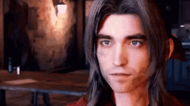 a man with long hair is standing in front of a table in a dark room .