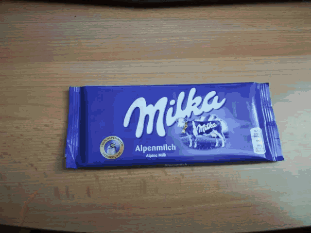 a purple milka alpenmilch chocolate bar is on a wooden table
