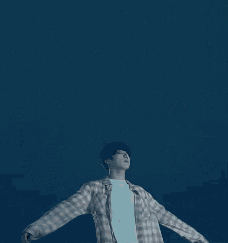 a man in a plaid shirt is standing with his arms outstretched in front of a blue sky .