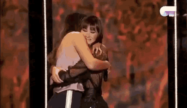 two women hugging each other on a stage in front of a microphone .