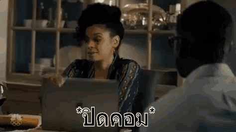 a woman is sitting at a table with a laptop computer and a man is standing behind her .