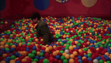 a man and a child are playing in a ball pit filled with colorful balls .