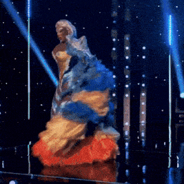 a drag queen in a blue and gold dress is dancing