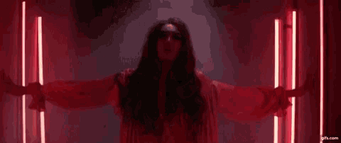a woman in a red dress is standing in a dark room with red lights behind her .