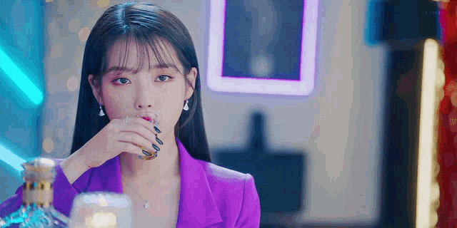 a woman in a purple suit is drinking from a glass while sitting at a table .