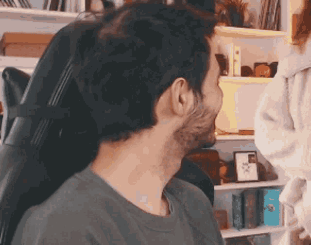 a man with a beard is sitting in a chair in front of a bookcase