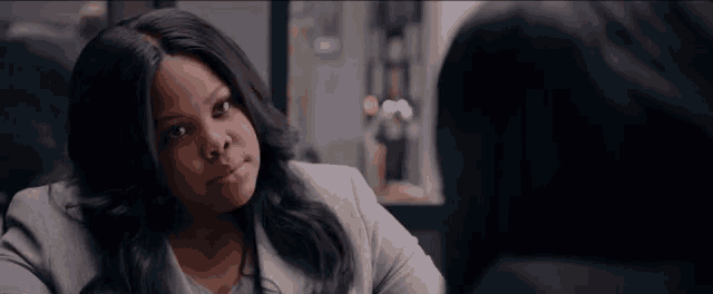 a woman is sitting at a table talking to another woman and looking at the camera .