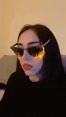 a woman wearing ray-ban sunglasses has flames coming out of her eyes