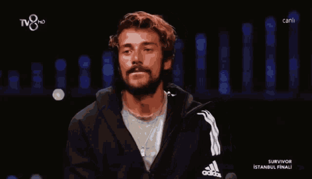 a man in a black adidas jacket is on a television screen