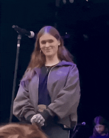 a woman in a purple jacket stands in front of a microphone on a stage