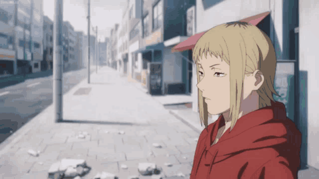 a girl in a red hoodie stands on a sidewalk in a city