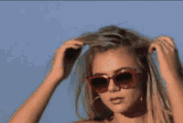 a woman wearing red sunglasses holds her hair in her hands