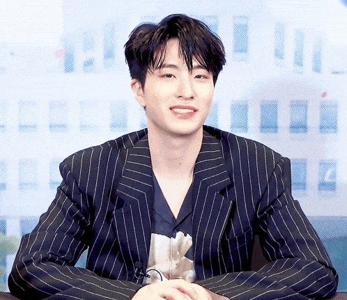 a young man wearing a striped suit is sitting at a table with his hands folded