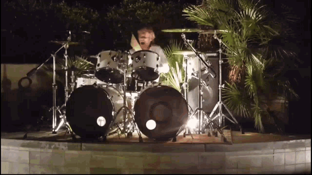 a man is playing drums in front of a palm tree at night