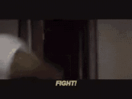 a man in a white shirt and black tie is standing in front of a door and says fight !