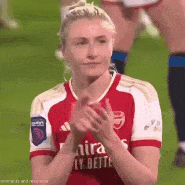 a woman in a red and white soccer jersey is clapping her hands on a soccer field .