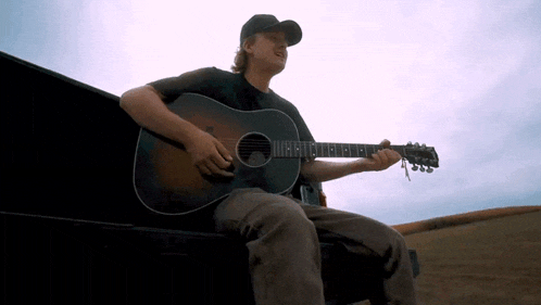 a man is playing an acoustic guitar while sitting in the back of a truck
