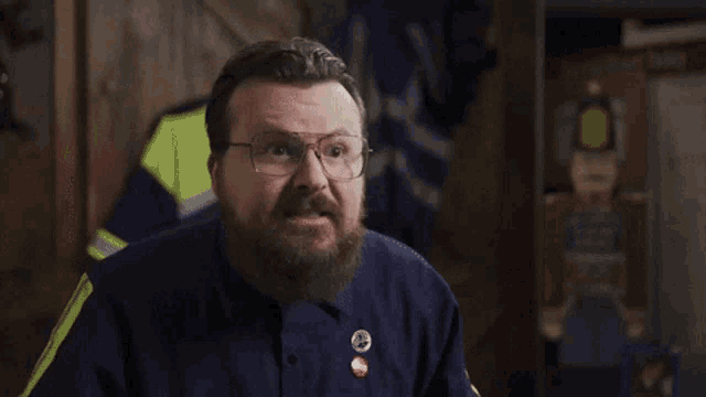 a man with a beard and glasses is wearing a blue shirt with a red button that says ' i love you '