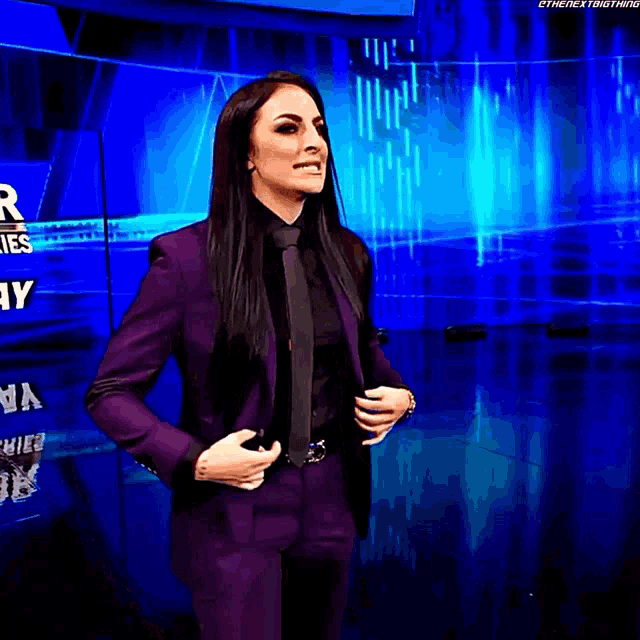 a woman in a purple suit and tie stands in front of a blue background .