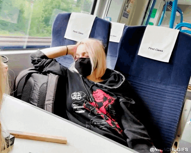 a woman wearing a mask is sitting in a first class seat on a train