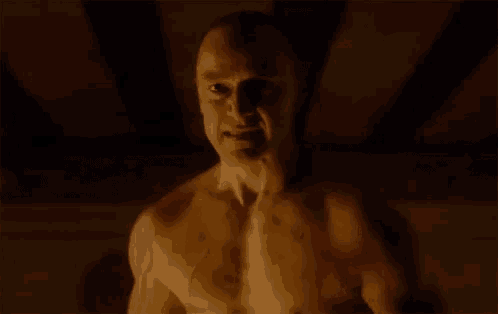 a shirtless man is making a face in a dark room .