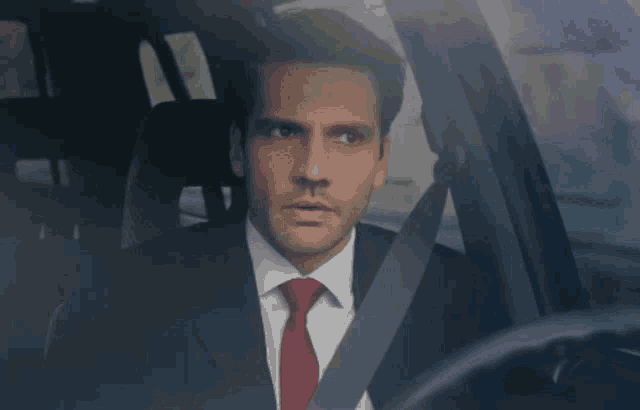a man in a suit and tie driving a car