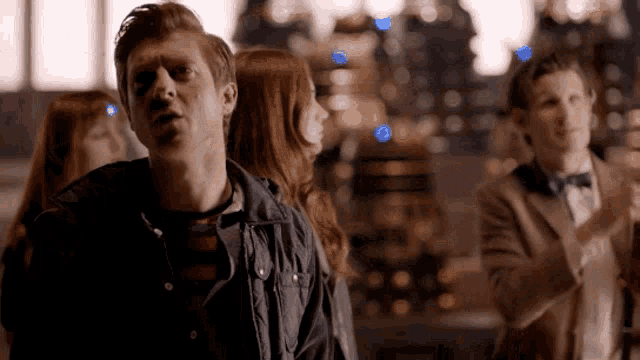 a group of people are standing in a room and one of them is wearing a blue jacket