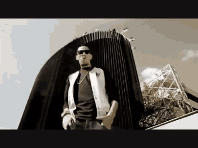 a man wearing sunglasses stands in front of a tall building