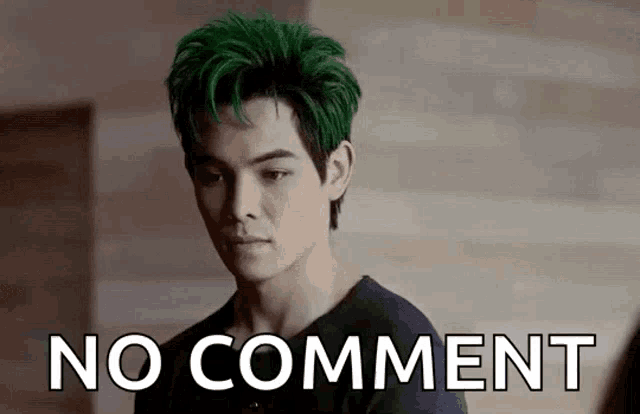 a man with green hair is standing in front of a wall with the words `` no comment '' written on it .